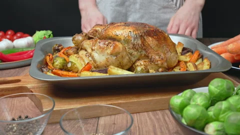 Placing on the table a whole grilled chicken in an oven pan with roast vegetable Stock Footage 145117261