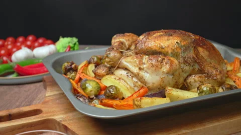 Placing on the table a whole grilled chicken in an oven pan with roast vegetable Stock Footage