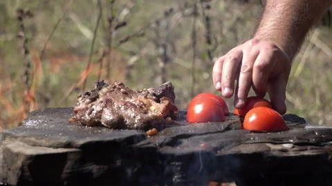 Placing Vegetables Next to Meat Grilling on Stone Over Campfire 動画素材 317888334