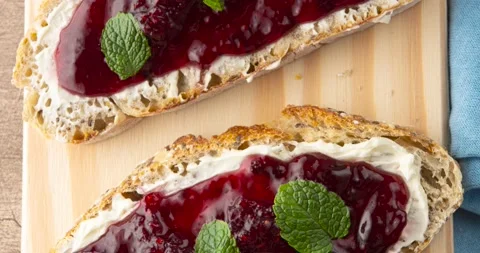 Plain bread, cream cheese, berries jam and mint leaves over wooden board. Stock Footage 194541130