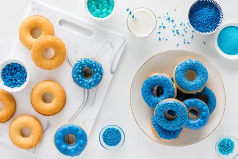 Plain donuts being decorated with blue candy chocolate and sprinkles. Stock Photos