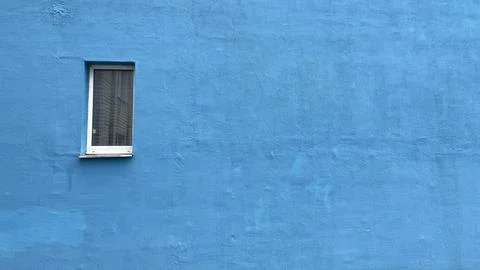 A plain, light-blue wall with a small white window is depicted. Foto stock
