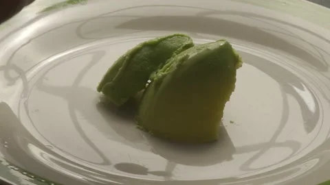 A plain white plate is displayed with pieces of a ripe avocado scattered on it Stock Footage 232804098