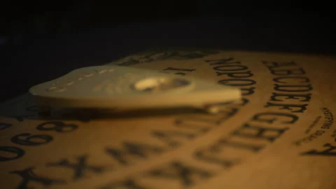 Planchette on a Ouija board in dim candlelight, letters visible on wooden Stock Footage 333522432