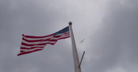 Plane appears through clouds, goes past flag, back into clouds Stock Footage 135441511