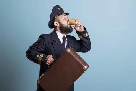 Plane captain drinking coffee and hurrying to go to work with suitcase Stock Photos