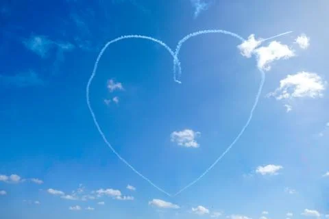 Plane doing acrobatic formation and creating a heart shape in the blue sky. Stock Photos