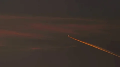 A plane flies against dramatic red sunset sky at twilight with illuminated trail Vídeos de archivo 94230583