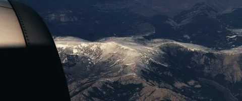 The plane flies over the snowy mountain peaks. View through an airplane window Stock Footage 127135505