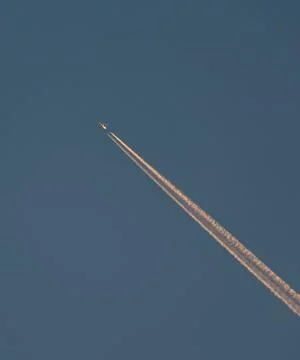 A plane flies through a clear sky, leaving a smoke trail behind Stock Photos