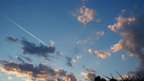Plane flies through a colorful sky filled with pink and gray clouds during sunse Stock Footage 341829534