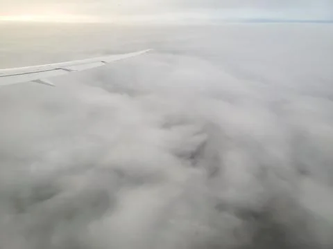 Plane flying high above cloud layer viewed from passenger cabin window Stock Photos