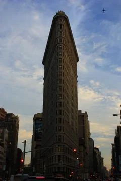 Plane flying over Flatiron building in clear blue sky during evening, sunset Stock Photos