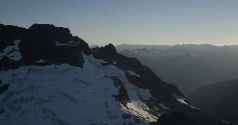 Plane flying over snowy rocky mountains during sunset Stock Footage
