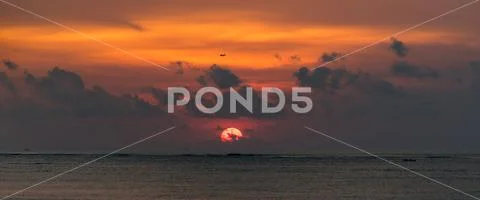 Plane flying over the Sun in a Bali sunset Stock Photos