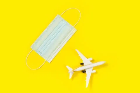 Plane model and face mask on a yellow background. Flight impact of coronaviru Stock Photos
