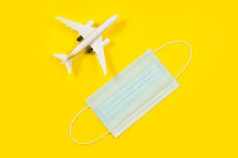 Plane model and face mask on a yellow background. Flight impact of coronaviru Stock Photos