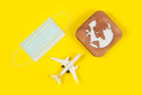 Plane model, face mask and earth model on a yellow background. Flight impact  Stock Photos