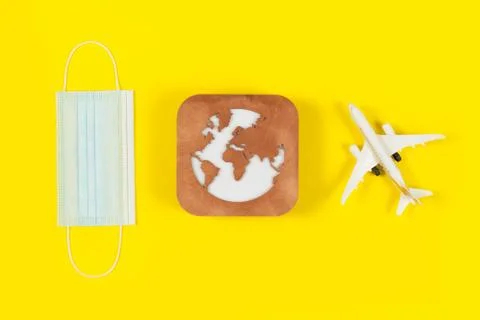 Plane model, face mask and earth model on a yellow background. Flight impact  Stock Photos