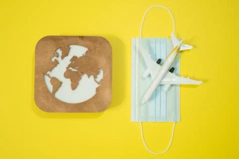 Plane model, face mask and earth model on a yellow background. Flight impact  Stock Photos