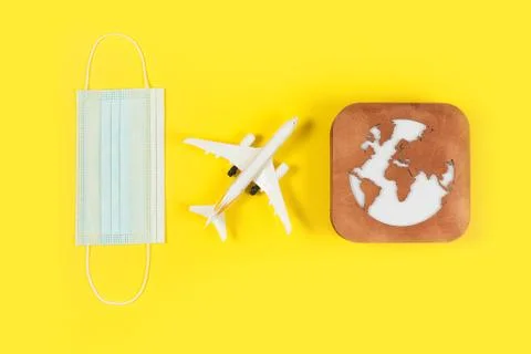 Plane model, face mask and earth model on a yellow background. Flight impact  Stock Photos