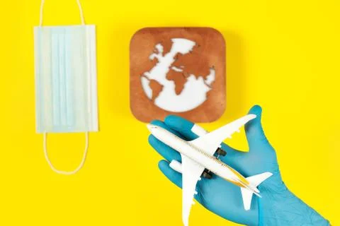 Plane model in hand, face mask  and earth model on a yellow background. Hands Stock Photos
