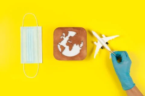 Plane model in hand, face mask  and earth model on a yellow background. Hands Stock Photos