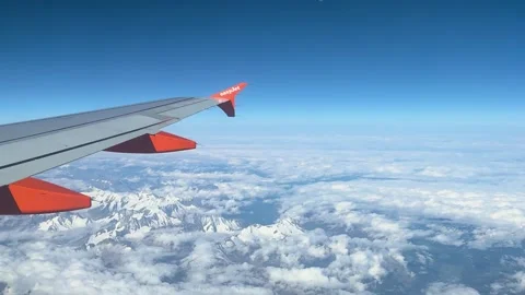 Plane passes majestically snow capped mountains beneath thick clouds blue sky Vídeo Stock 320844928