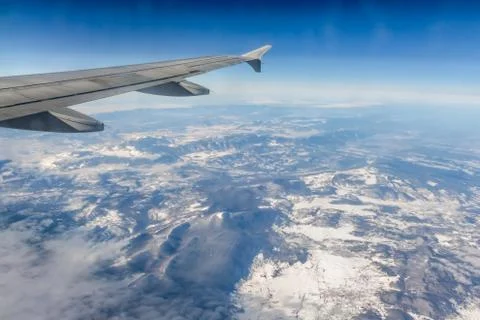 Plane silver wing during a flight over white clouds and a winter land is on t Stock Photos