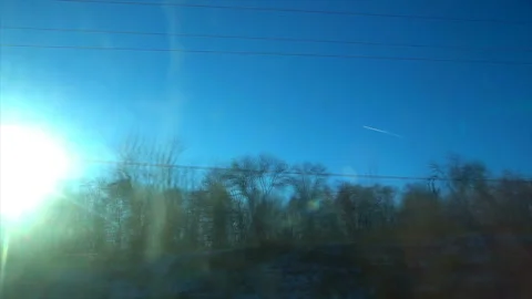 Plane in the sky against the backdrop of bright winter sun, view from the train Stock Footage 99429347