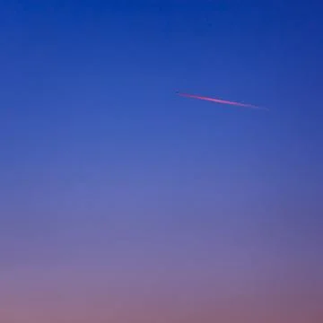 The plane in the sky is illuminated by the rays of the rising sun. Stock Photos