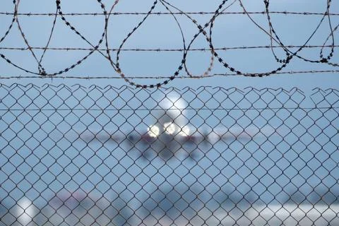 Plane taking off behind barbed wire fence, selective focus on wire. Stock Photos