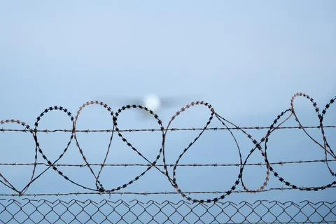 Plane taking off behind barbed wire fence, selective focus on wire. Stock Photos