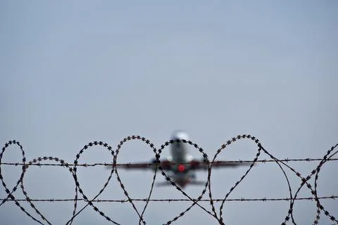 Plane taking off behind barbed wire fence, selective focus on wire. Stock Photos
