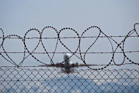 Plane taking off behind barbed wire fence, selective focus on wire. Stock Photos