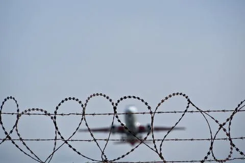 Plane taking off behind barbed wire fence, selective focus on wire. Stock Photos