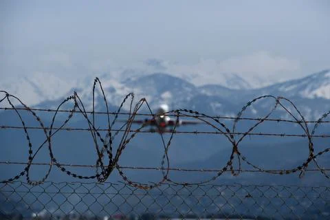 Plane taking off behind barbed wire fence, selective focus on wire. Stock Photos