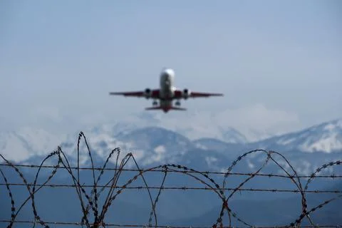 Plane taking off behind barbed wire fence, selective focus on wire. Stock Photos