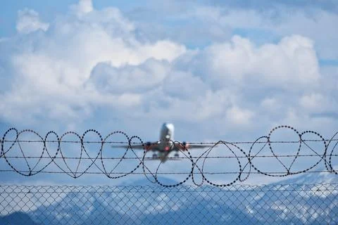 Plane taking off behind barbed wire fence, selective focus on wire. Stock Photos