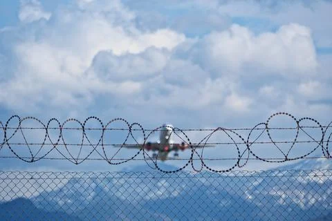 Plane taking off behind barbed wire fence, selective focus on wire. Stock Photos