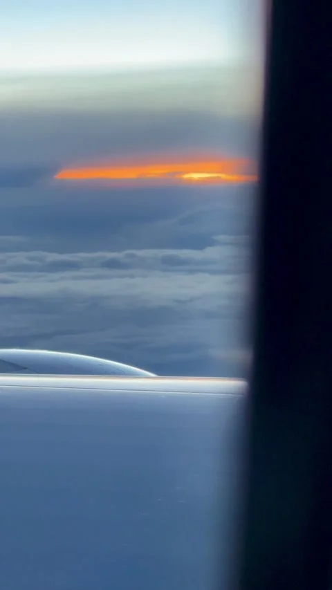 Plane window view of a narrow orange sunset glowing beneath dark clouds, with Stock Footage 345969513