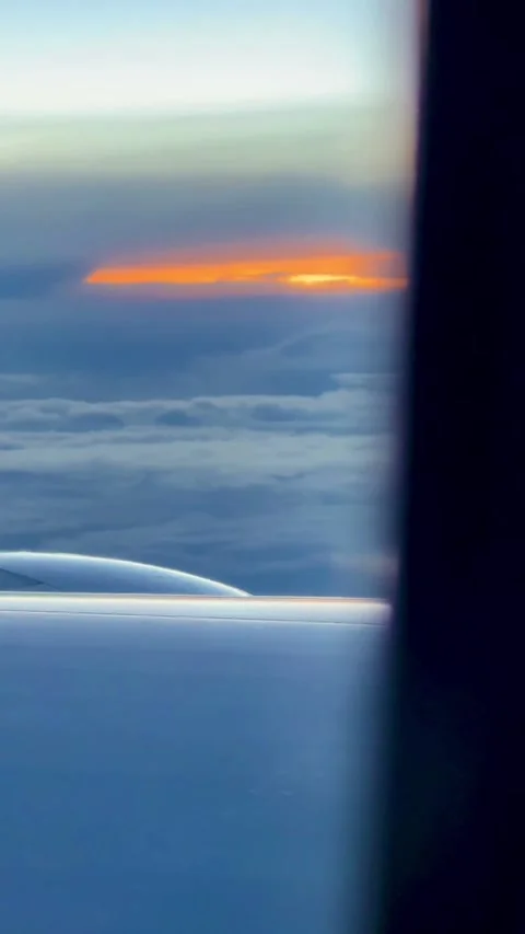 Plane window view of an orange sunset glowing between layers of clouds, with Stock Footage 345969554