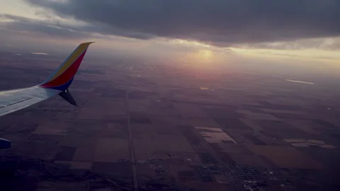 Plane window view of sun setting over farmland and a town Stock Footage 348791331