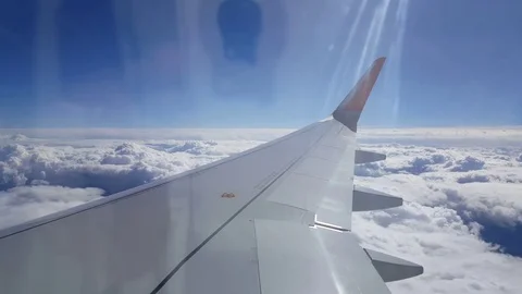 Plane wing in flight above clouds, sunlight flare, blue sky Stockbeeldmateriaal 74665891
