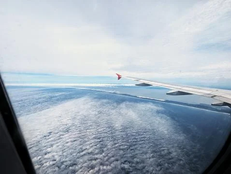 Plane wing over ocean clouds at sunrise. Suspended over sea with view Stock Photos
