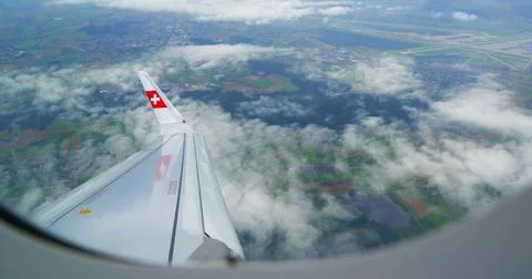 Plane wing viewed from window during flight over fields and clouds near airport Stock Photos