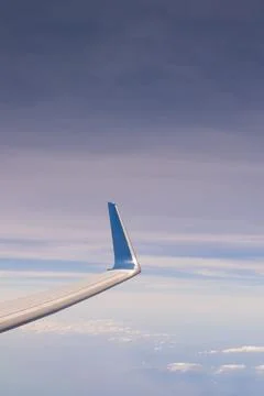 A plane wing is visible outside a window as it flies above white clouds and.. Stock Photos