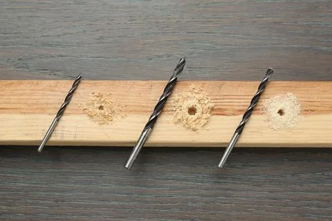 Plank with holes, drill bits and sawdust on wooden table, flat lay Stock Photos