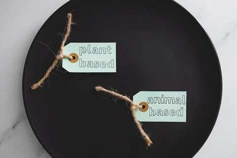 Plant-based and animal-based product tags on top of black dining plate on mar Stock Photos