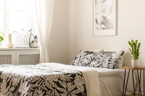 Plant on table next to bed with patterned sheets in bright bedroom interior w Foto stock